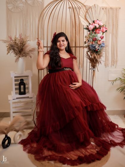 A seated portrait in our maroon ruffled gown, showing its volume and flow. The studio props like the birdcage add a whimsical touch.
