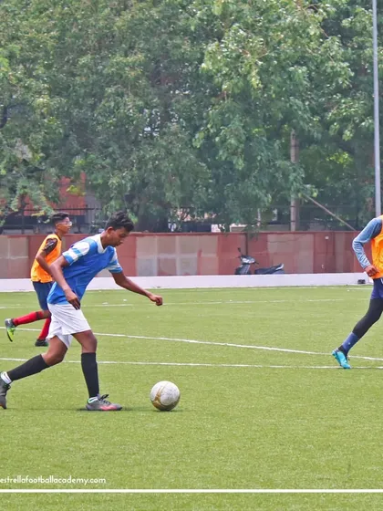 A player in a blue jersey advances the ball up the field during a trial match, demonstrating his control and awareness.