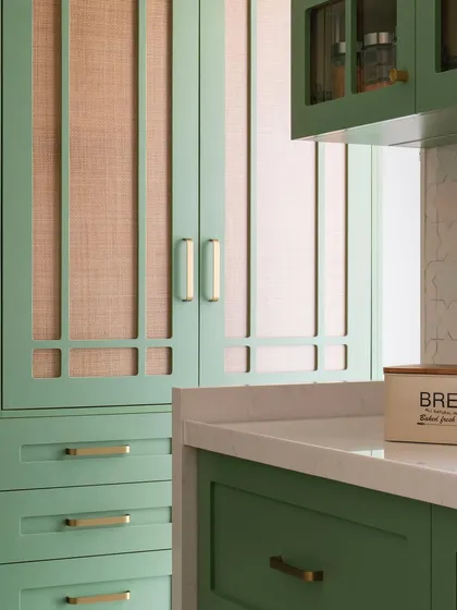 This kitchen has a quiet personality, defined by its soft green cabinetry and brushed brass handles. The addition of cane on the pantry doors adds a layer of warmth and texture, creating a space that feels fresh and easy to be in.