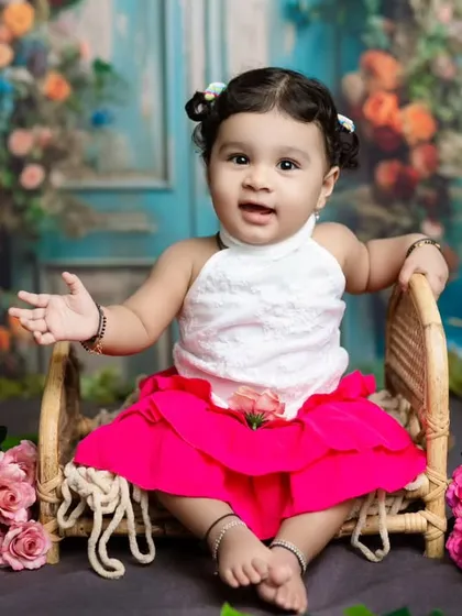 This little cutie is sitting up in a miniature chair, surrounded by a floral backdrop, looking ready for her close-up.