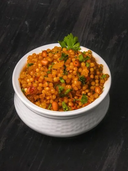 A bowl of sabudana khichdi, a traditional Indian breakfast dish, garnished with fresh parsley. The dark wooden background provides a rustic and authentic setting.