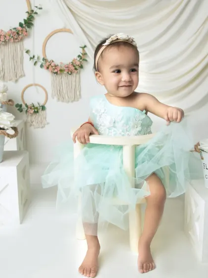 A happy baby girl in a mint green tulle dress. This portrait captures her bright personality and the delicate details of her outfit.