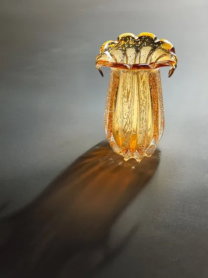 Where light dances on glass. This amber-toned, fluted glass vase casts a beautiful, dramatic shadow, showcasing its intricate texture and form. It is the art piece your home has been waiting for.