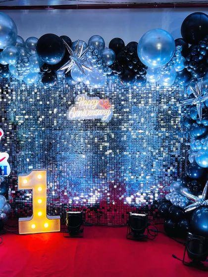 A sleek and modern backdrop with a silver shimmer wall. The black and metallic blue balloon frame, along with a light-up number '1', creates a stylish and eye-catching decoration for a first birthday.