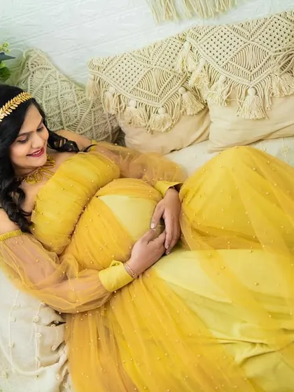 A serene portrait of a mom-to-be relaxing on our boho studio couch in a beautiful yellow gown.