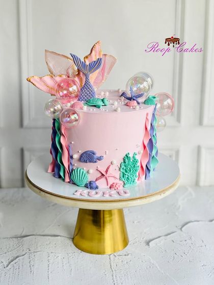 An enchanting mermaid cake with under-the-sea details. This pink cake is decorated with a mermaid tail, seashells, coral, and shimmering gelatin bubbles for a magical ocean vibe.