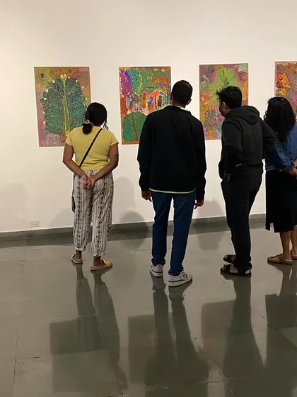 Visitors looking at the colorful, dense paintings by Devu Nenmara.