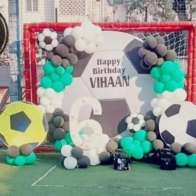 An outdoor football theme party on a turf, with a goalpost, a large football backdrop, and balloon decorations for Vihaan's 6th birthday.