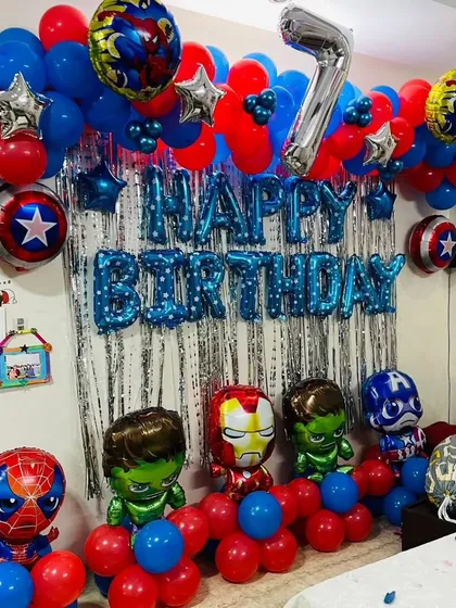 A superhero themed birthday party for a 7-year-old. This home setup includes a silver fringe backdrop, 'Happy Birthday' foil balloons, and character balloons of the Avengers like Spider-Man, Hulk, and Iron Man.