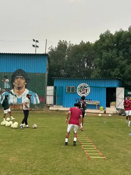 A typical training day at our academy. Players engage in passing drills under the watchful eye of our coaches, with the iconic mural of football legends inspiring them in the background.