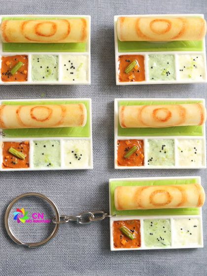 A batch of realistic dosa miniatures on platters, ready to be turned into magnets or keychains.