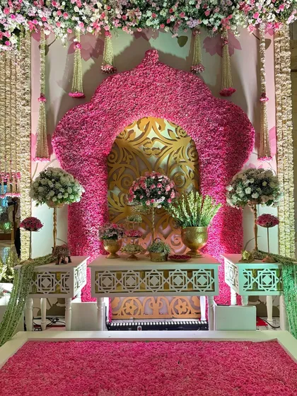 A stunning photo-op corner featuring a floral arch against a gold-patterned backdrop. The floor is a carpet of fresh pink petals, creating a truly immersive experience.