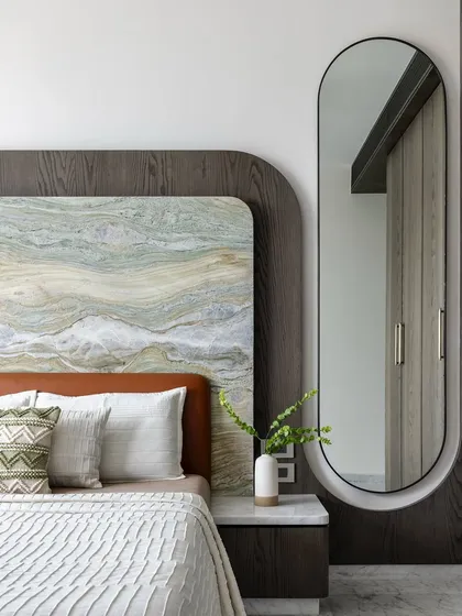 We love layering textures to create warmth and depth. This bedroom features a headboard combining a dramatic stone slab with a dark wood frame and a soft leather base, creating a rich tactile experience.