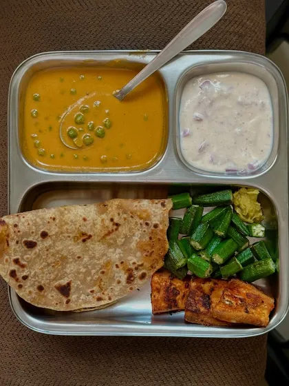 This plate has chapati, green peas curry, paneer, sautéed okra, and raita. It's a well-rounded vegetarian meal with multiple sources of protein and fiber.