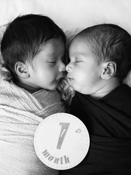 A black and white portrait of one-month-old twins sleeping nose-to-nose, capturing their incredible bond from the very beginning.