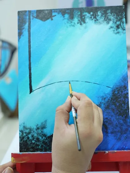 A close-up of a participant painting a night sky. The fine details, like the stars and trees, bring the scene to life.