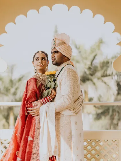 A regal portrait of the couple on a balcony overlooking a beautiful landscape. The groom holds sunflowers, a personal touch from their first look.