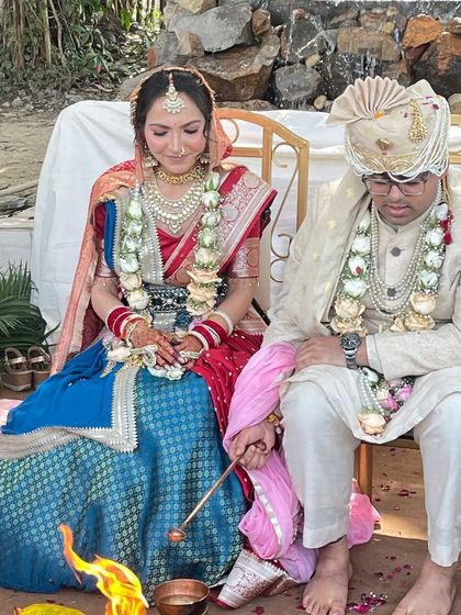 A candid moment from a wedding ceremony, showcasing the bride in her beautiful Tehhzeeb Couture lehenga. The combination of red and blue with traditional fabrics creates a look that is both classic and unique.