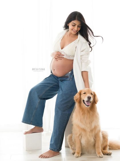 A relaxed and modern maternity portrait. The mother-to-be shares a happy moment with her golden retriever, showcasing a casual and authentic family bond.