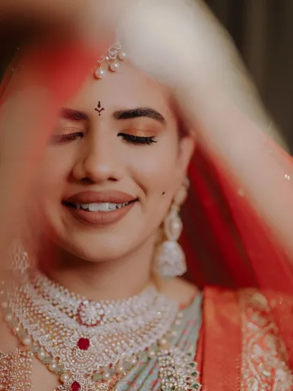 A close-up of this bride's serene expression. The soft, warm tones on her eyes and a natural lip color create a gentle yet beautiful look, peeking through a delicate red veil.