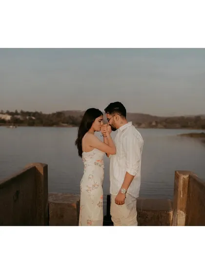 A wide shot of a couple sharing an intimate moment on a pier, with the expansive lake and hills creating a beautiful backdrop.