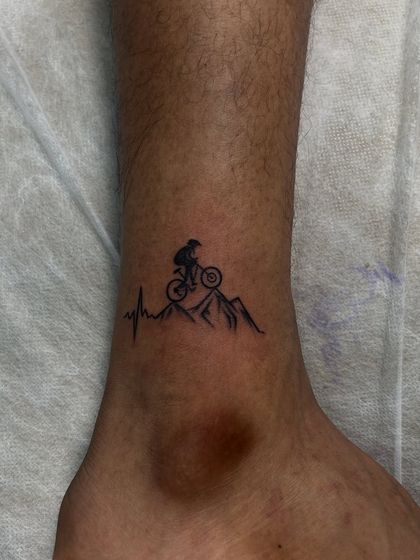 For the mountain biker. This small tattoo combines a heartbeat line with a biker on a mountain, symbolizing a passion that makes the heart race.