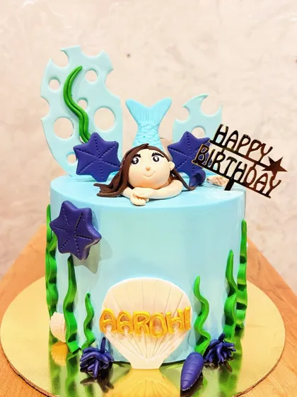 A simple and sweet mermaid-themed cake with a fondant mermaid peeking out of the water.