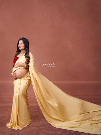A profile shot that beautifully showcases the baby bump with a modern saree drape. The flowing fabric adds movement and a touch of glamour to this traditional concept.