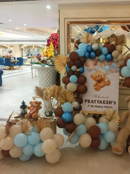 A beautiful welcome corner for the teddy bear party, featuring a personalized sign, a large stuffed bear, and a balloon garland with dried palm leaves for a rustic touch.