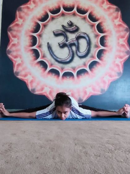 In a full split forward bend, or Samakonasana, in front of an Om mural. This pose represents the journey of yoga: a journey of the self, through the self, to the self.
