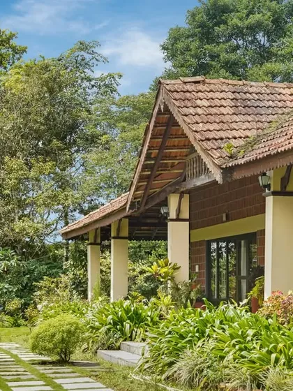 The beautiful architecture of Villa Magnolia, with its sloping tiled roof and supportive pillars, surrounded by a vibrant, well-maintained garden.