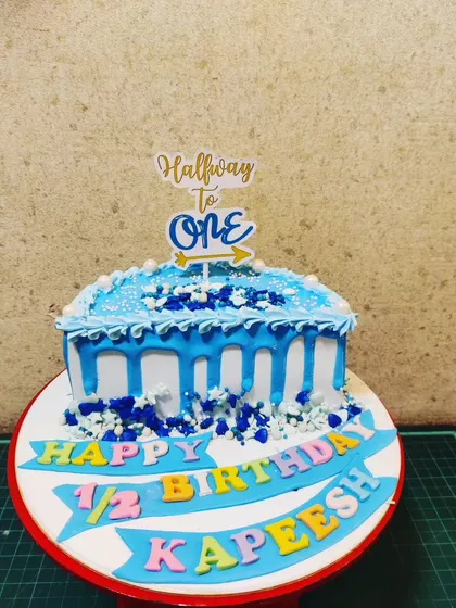 Another take on the half-birthday, this "Halfway to One" cake features a blue drip design and a celebratory banner for a baby boy.