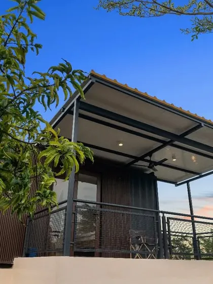 A container villa at Suzo Farms, viewed through the leaves of a mango tree. This shot emphasizes the home's connection to its agricultural setting, blending modern living with the beauty of the farm.
