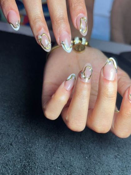 A close-up of the abstract gold line and pearl design, showing the delicate details on these oval-shaped nails.