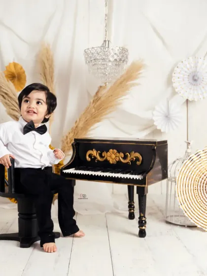 A dapper little gentleman dressed in a bow tie for his 'Pianist' themed session. He poses with a miniature piano, creating a classic and charming toddler portrait.