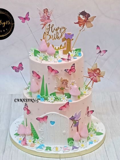 A whimsical two-tier fairy house cake. The pink cake features a fondant door, mushrooms, and fluttering fairies, creating an enchanting scene for a first birthday.