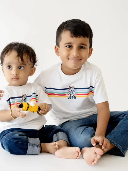 A sweet studio portrait of two brothers in matching shirts. The older brother has his arm around his younger sibling in a classic, heartwarming pose.