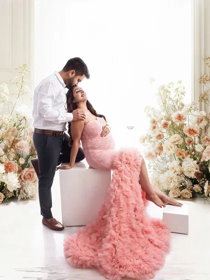 A romantic and tender pose with the partner gently kissing the mom-to-be's shoulder. The beautiful floral setting and soft pink gown create a fairytale-like atmosphere.