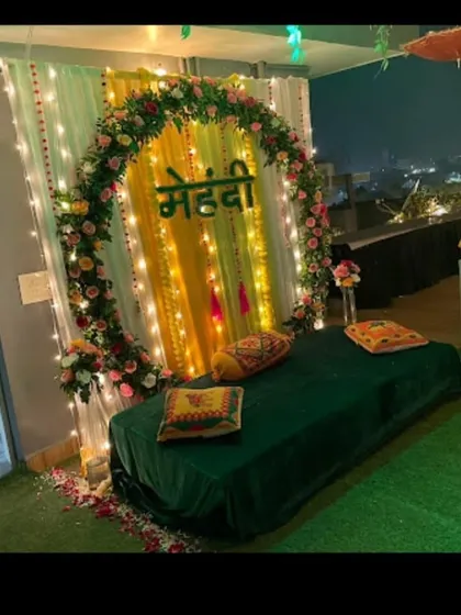 A beautiful rooftop Mehandi setup for an evening function. The floral ring backdrop is lit with fairy lights, and the low gadda seating creates a relaxed and intimate atmosphere.