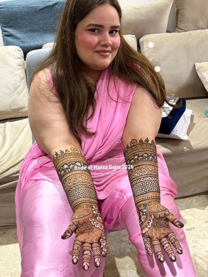 A happy bride showcasing her full-arm, band-style mehendi. Her smile shows her satisfaction with the intricate and symmetrical design that she chose for her special day.