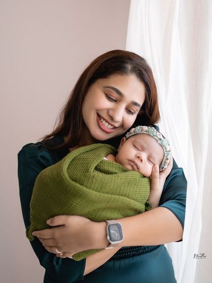 A mother smiling as she holds her sleeping newborn, wrapped in a cozy green swaddle.