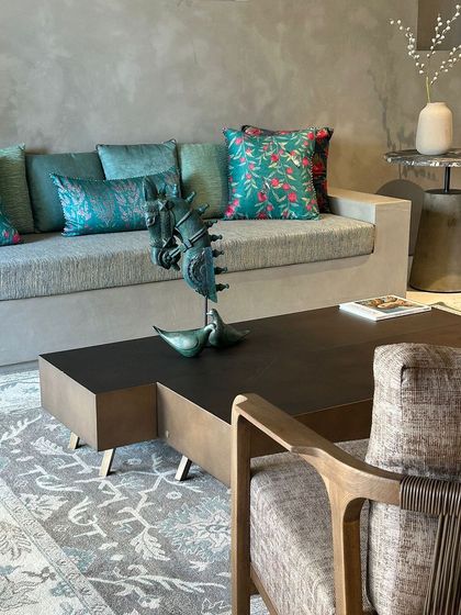 A close-up of the living space, showing the interplay of textures. A concrete-finish sofa is adorned with rich teal cushions, while a sculptural object sits on the modern coffee table.