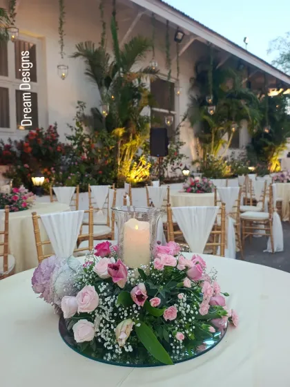 A beautiful centerpiece featuring pink roses and tulips. The arrangement sits on a mirrored base, reflecting the candlelight and adding a touch of romance to the guest tables.