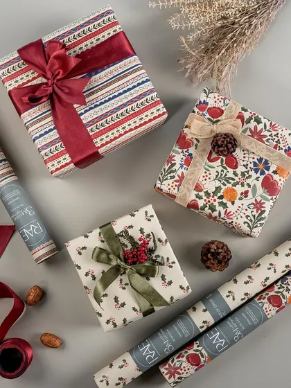 A festive flat lay of beautifully wrapped Christmas gifts using Rae's wrapping paper. The composition includes rolls of paper and natural elements like pinecones, creating a warm and inspiring holiday gifting scene.