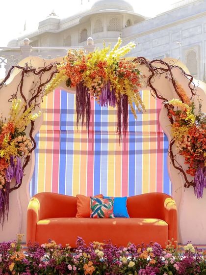A close-up of the main stage with a bright orange sofa. The backdrop of colorful stripes and an arch of branches and flowers perfectly frames the seating area for the couple.