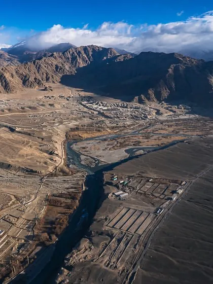 An aerial view of the high-altitude desert landscape surrounding Leh, Ladakh. The image shows the stark beauty and settlement patterns in this remote Himalayan region.