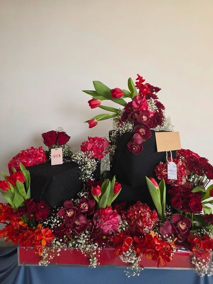 This shot captures the entire red-themed arrangement, showcasing the different levels and textures created with various blooms like tulips, carnations, and orchids.