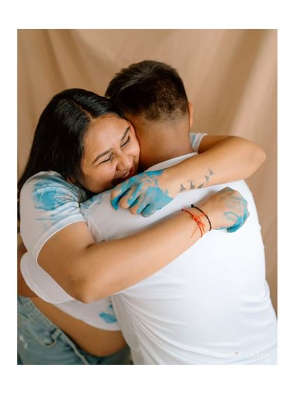 A huge, happy hug covered in paint! This shot captures the pure joy and fun of a creative gender reveal or baby announcement session.