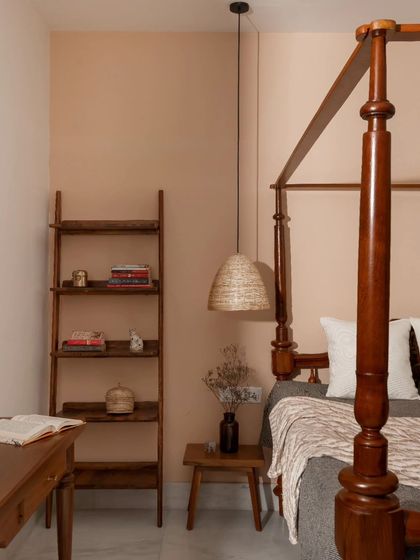 The bedroom continues the theme of traditional warmth with a four-poster teak bed. The walls are finished in a muted pastel color, creating a calm and restful sanctuary.