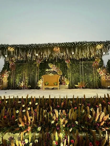 This wide shot captures the full splendor of the reception stage. The combination of a green wall, hanging florals, and a foreground of pampas grass creates a rich, layered, and utterly luxurious visual.